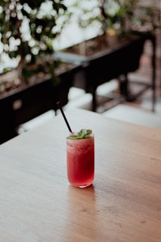 A refreshing glass of herbal drink surrounded by fresh herbs and fruits on a wooden table.