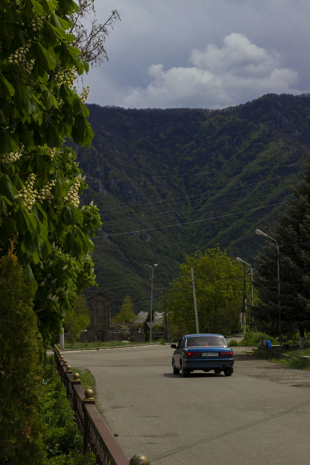 a car driving down a street next to a lush green hillside