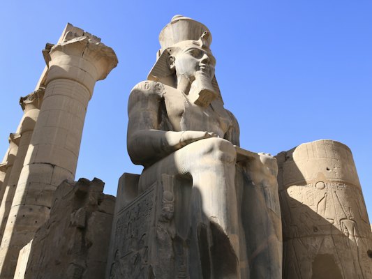 A statue of a man sitting in front of two tall pillars — Luxor, Egypt