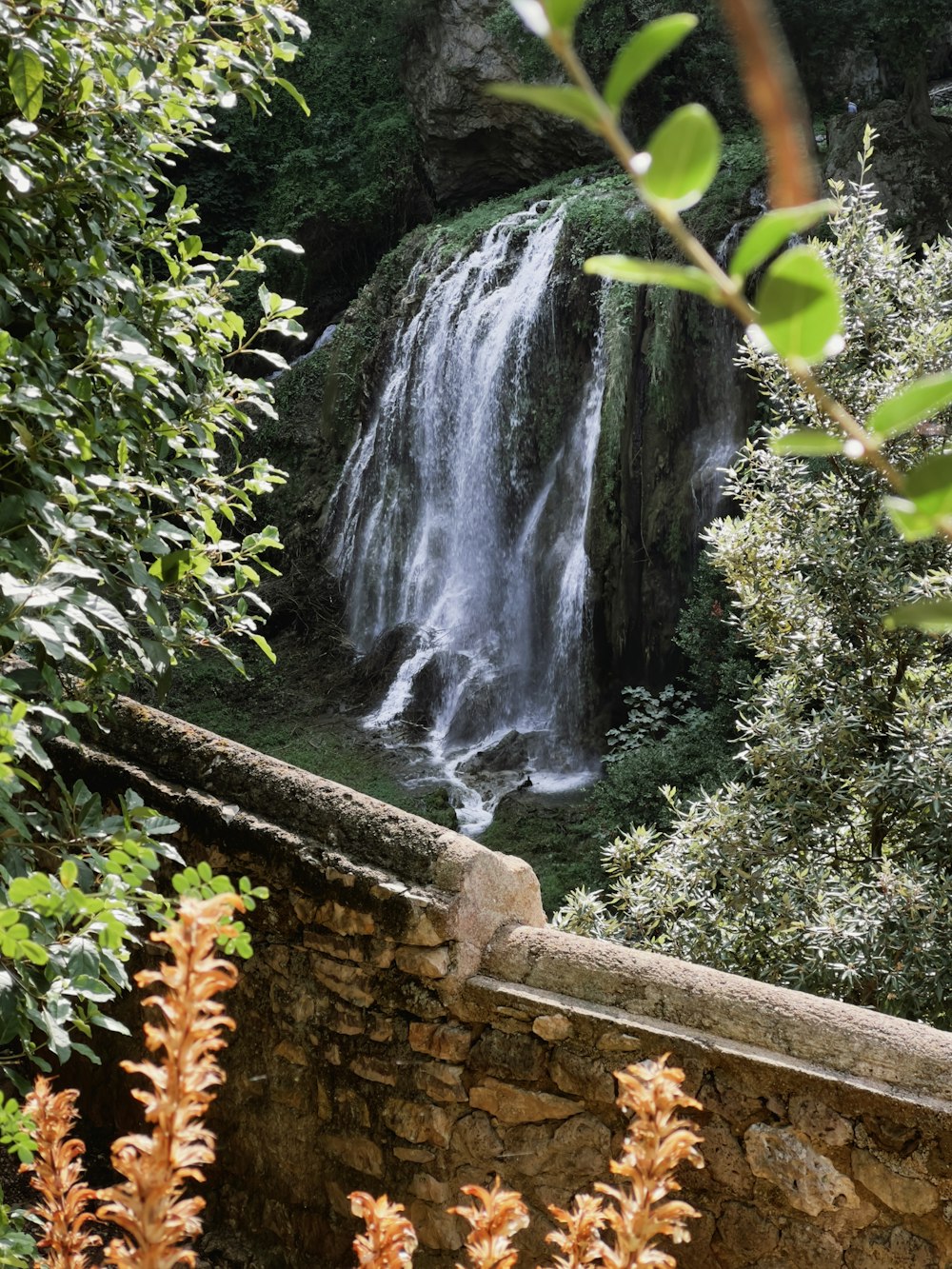 a view of a waterfall from behind a stone wall