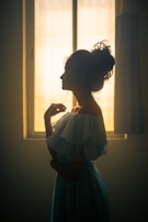 A model wrapped in a flowing black silk robe, standing by a softly lit window.