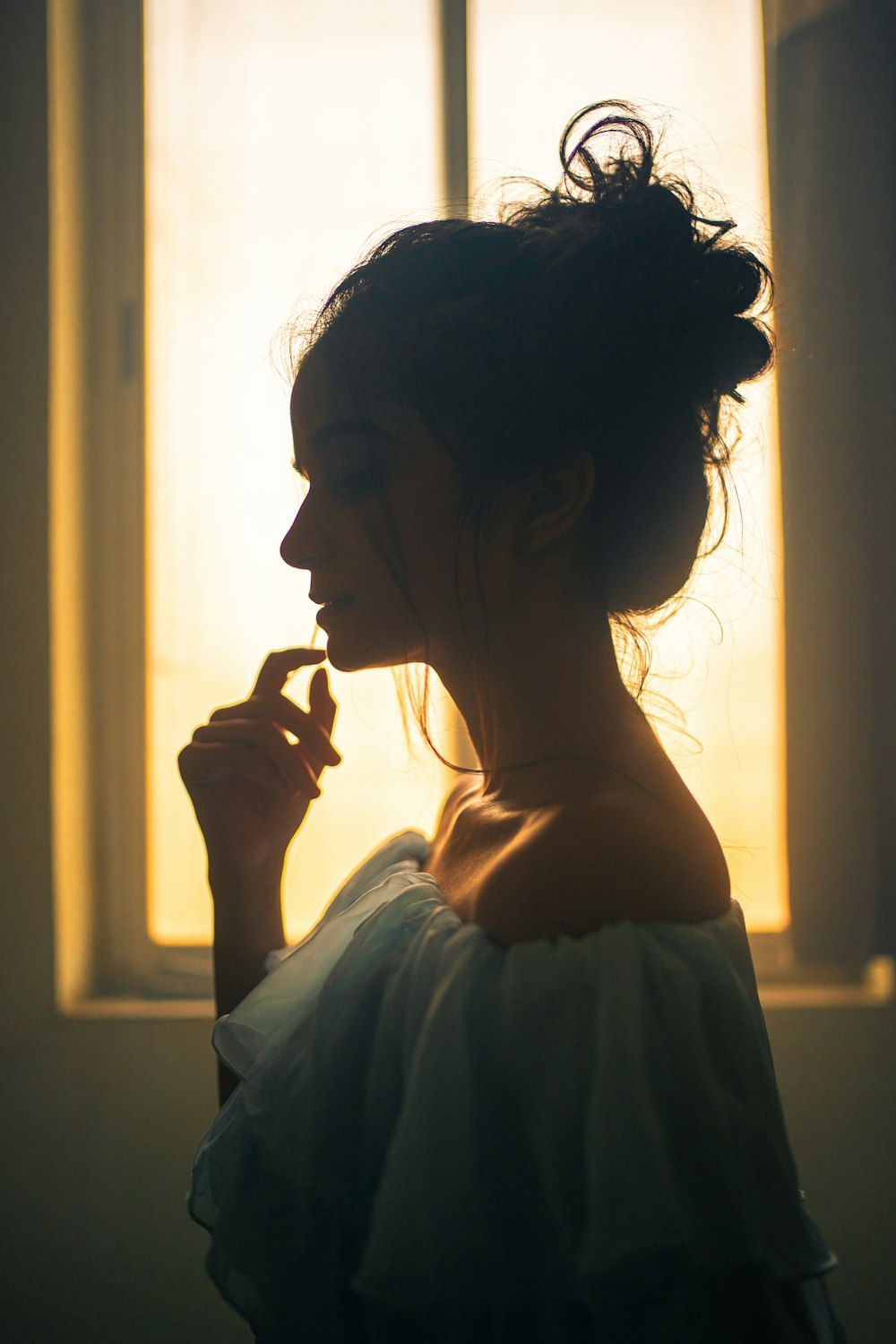 a woman standing in front of a window holding a cigarette