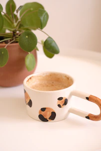 Close-up of a pastel-colored mug with a subtle, cute design sitting beside a small succulent plant.