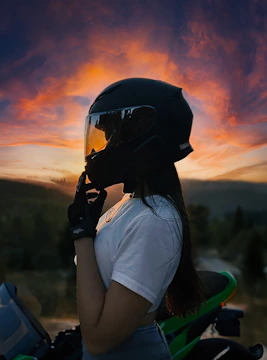 A group of women riders in black and red gear standing beside their motorcycles under a fiery sunset.