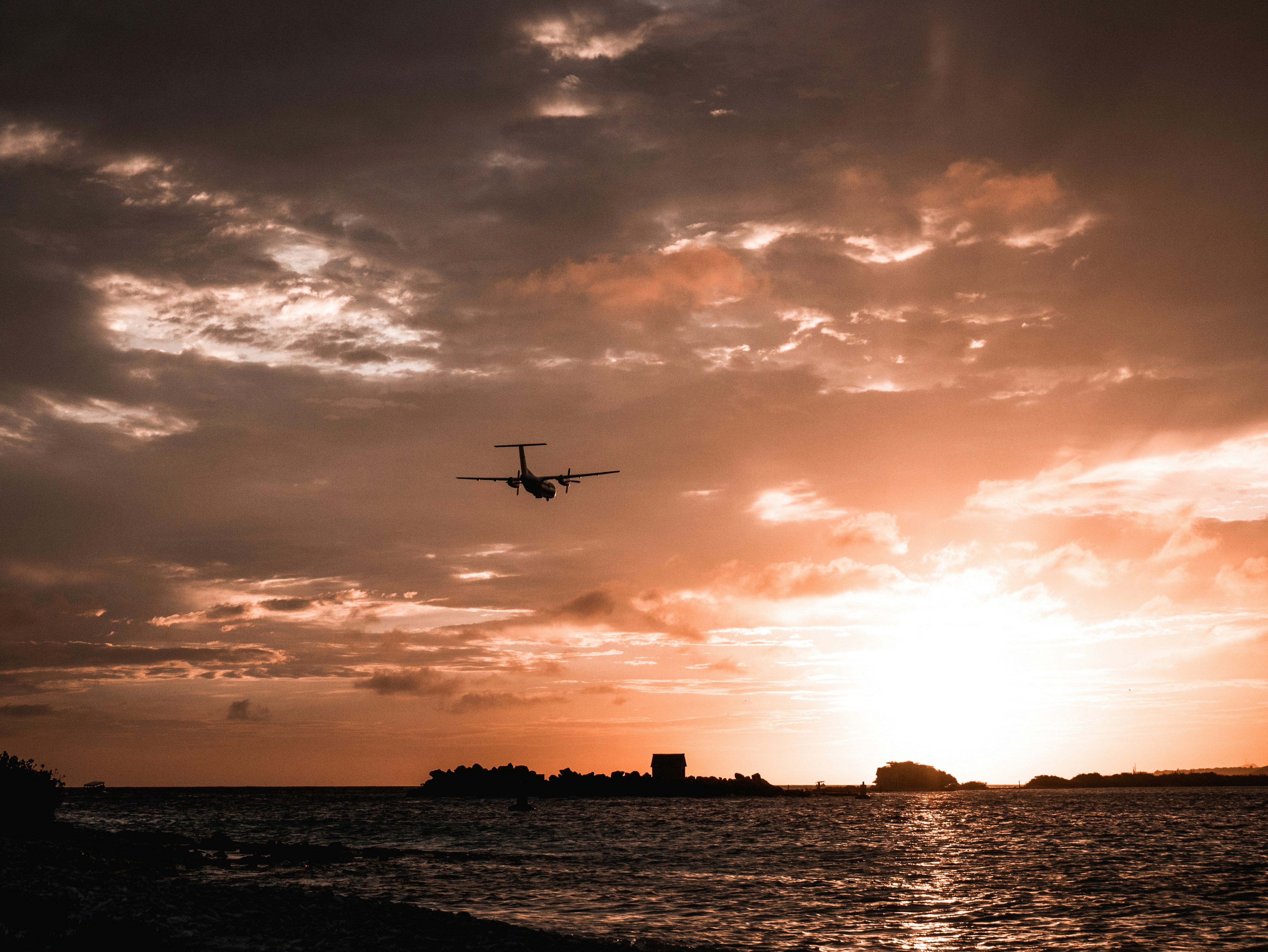 a plane flying over a body of water at sunset, 