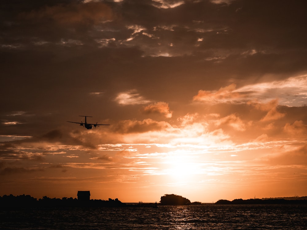 a plane flying over a body of water at sunset