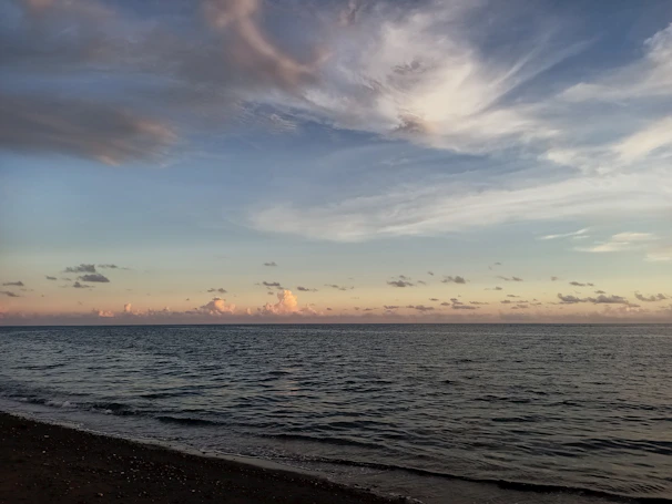 A wide shot of a calm beach at sunset, with gentle waves and pastel skies.