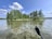 Close-up of a kayak paddle dipping into crystal-clear lake water surrounded by lush greenery.