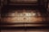 An ornate wooden balcony with intricate carvings and patterned glass panels. The woodwork features geometric shapes and decorative details, creating a sense of sophistication and historical elegance.