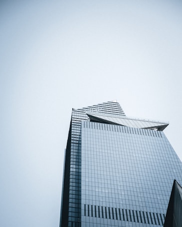 A modern skyscraper with a glass facade, showcasing a geometric and angular design. The building has a sleek, futuristic appearance with reflective surfaces that create a pattern.