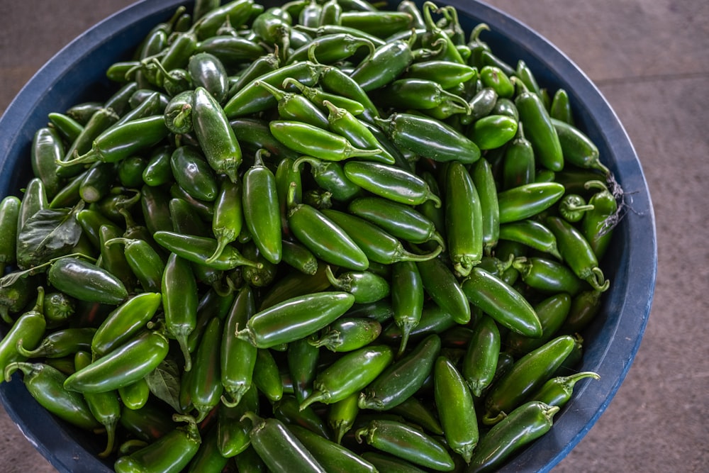 a blue bowl filled with green peppers on top of a table