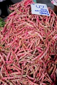 A large pile of fresh, mottled pink and green beans with a handwritten sign displaying a price. The beans are heaped in an abundant display, likely at a market setting.