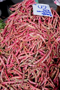 A large pile of fresh, mottled pink and green beans with a handwritten sign displaying a price. The beans are heaped in an abundant display, likely at a market setting.
