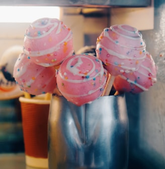 a group of pink frosted donuts sitting on top of a metal cup