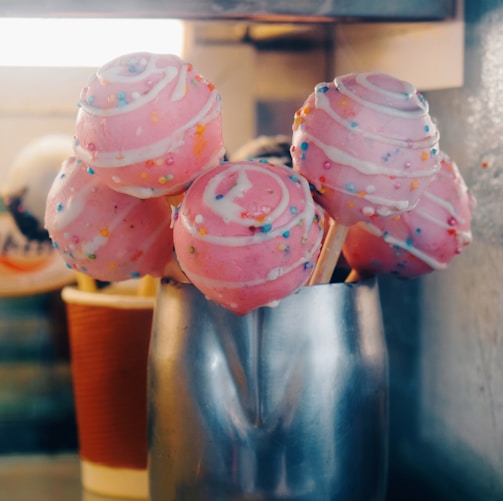 a group of pink frosted donuts sitting on top of a metal cup