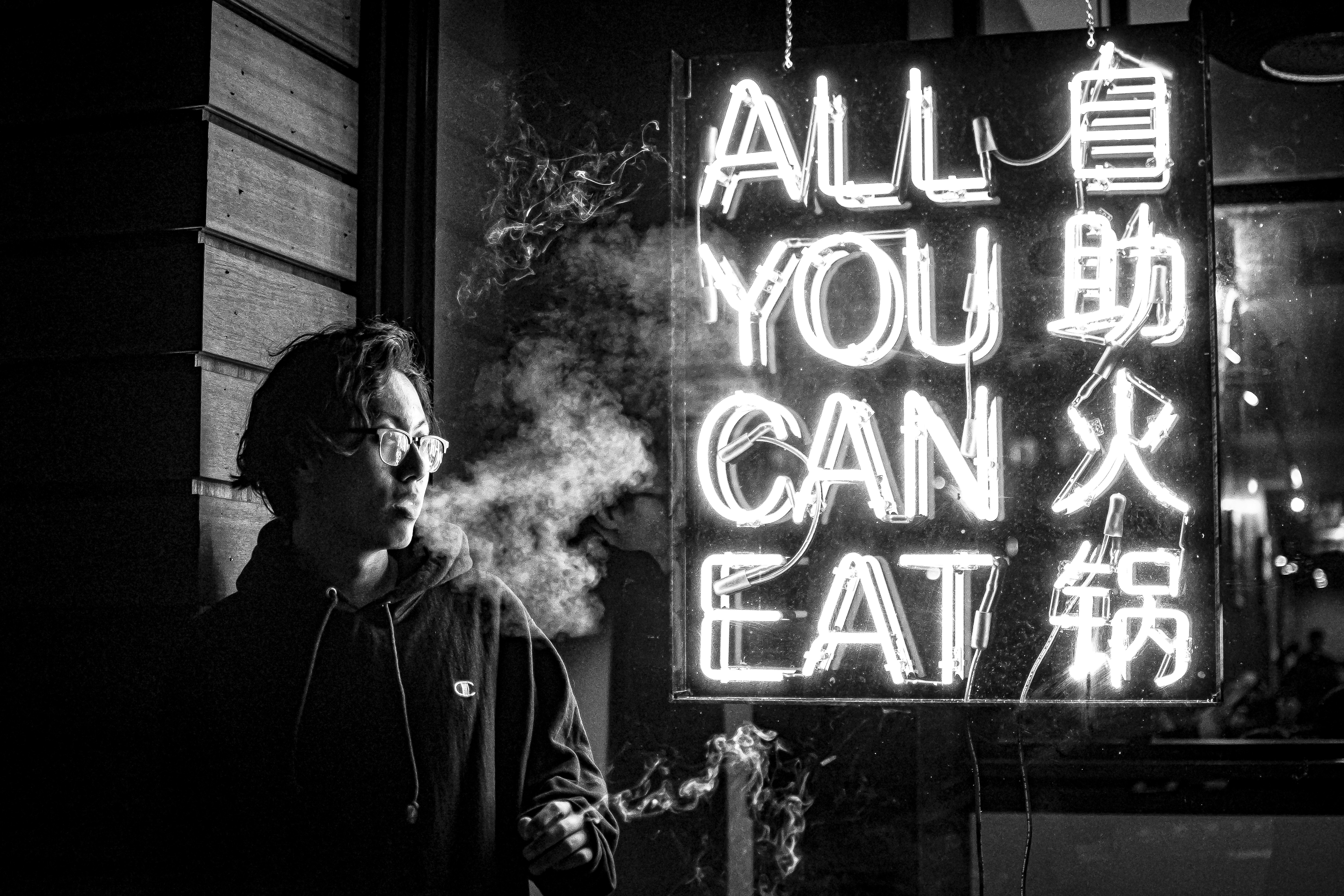 a man smoking a cigarette in front of a neon sign