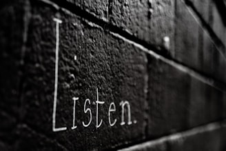 a black and white photo of the word listen written on a brick wall