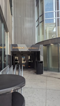 A building entrance labeled 'Scotiabank Premium Entrance' features modern architecture with glass panels and metallic accents. The area includes a railing and a trash can, with multiple doors at the entry.