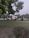 A well-maintained garden with lush green grass and neatly trimmed bushes. In the background, there is a light-colored decorative structure with arches, surrounded by more greenery. The sky appears overcast and there are tall trees with dense foliage.
