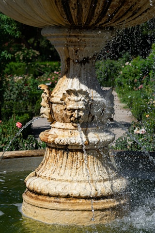 Close-up of a meticulously crafted stone fountain surrounded by lush greenery and delicate flowers.
