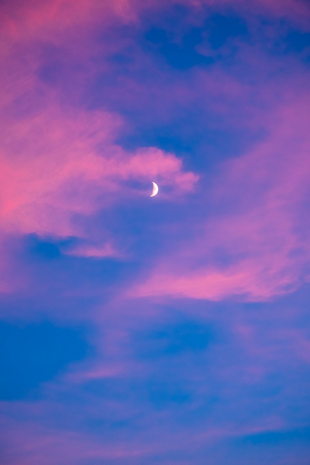 a pink and blue sky with a half moon