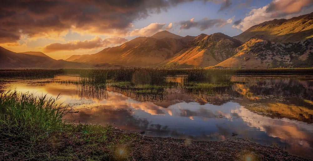 a lake surrounded by mountains under a cloudy sky