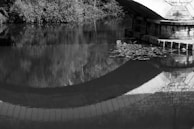 A black and white photo of an old bridge reflected perfectly in calm water.