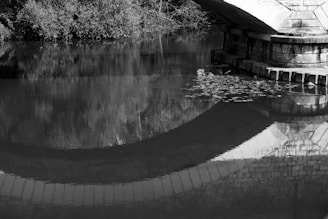 A black and white photo of an old bridge reflected perfectly in calm water.