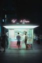 a couple of people standing outside of a food stand