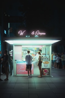 Night view of the storefront illuminated, with customers picking up ice late into the evening.