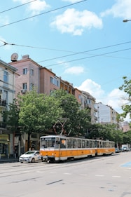 a yellow and white bus driving down a street next to tall buildings