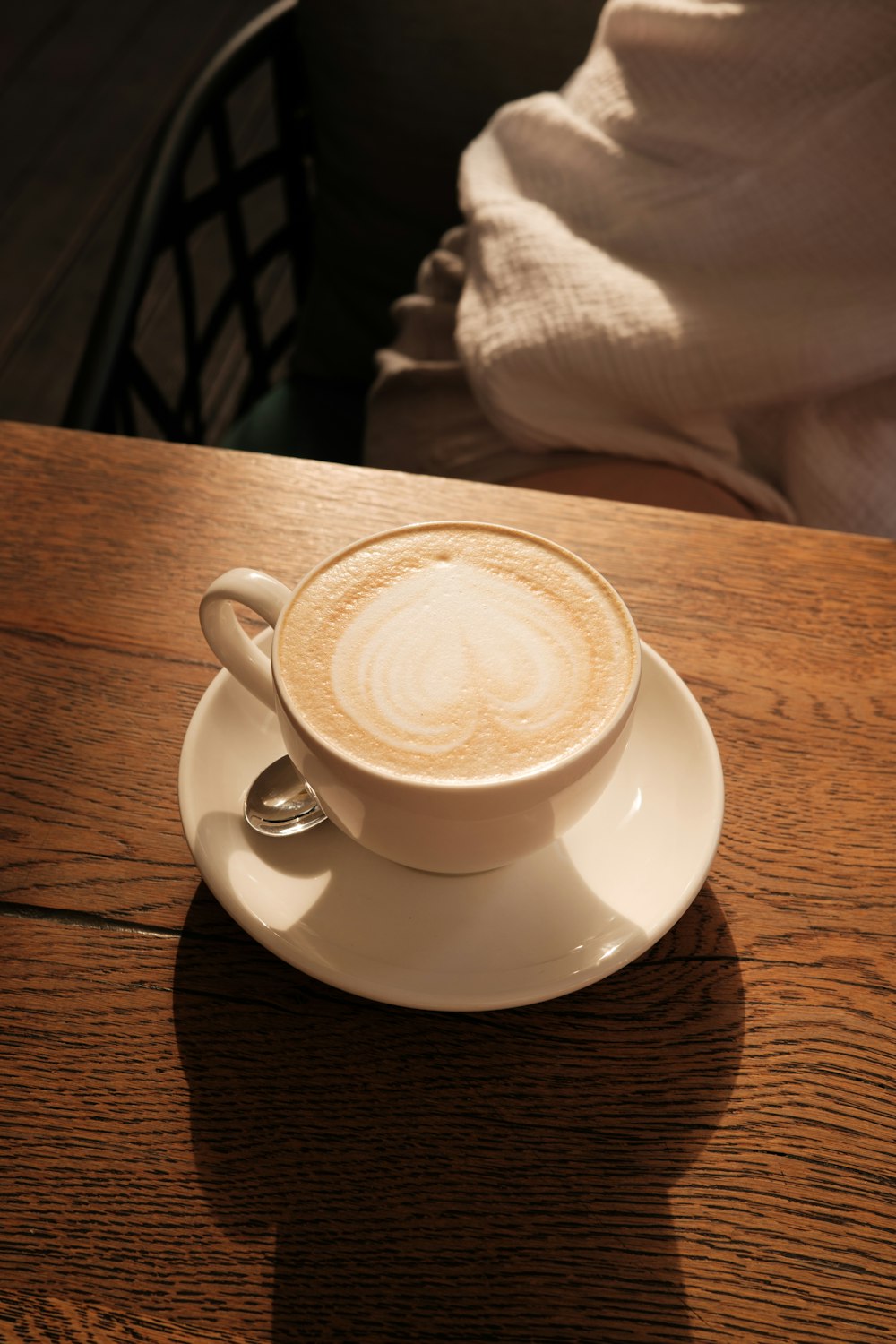 a cappuccino sits on a saucer on a wooden table