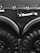 A close-up view of a large vehicle's wheels and bodywork, featuring thick black tires with deep treads. Above the wheels, there is a matte black surface with metal fasteners and a white-handled tool, possibly an axe, mounted horizontally.