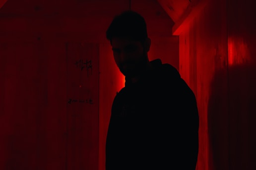 A shadowy figure in a dimly lit room surrounded by old classified files and glowing red neon symbols.