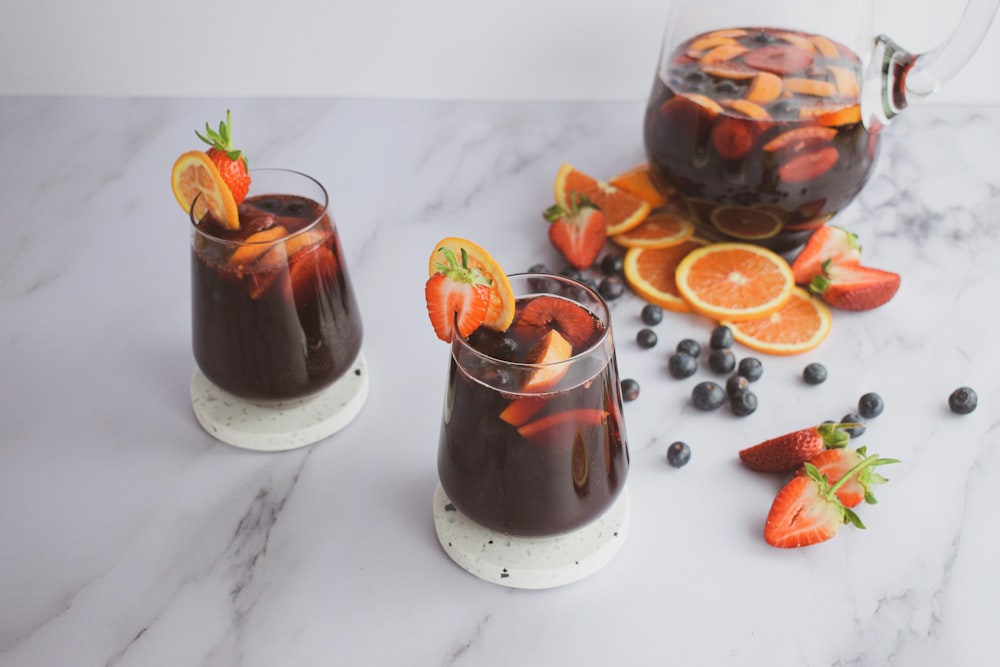 two glasses filled with liquid and garnished with fruit