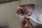 A person is using a metal nail clipper to trim their fingernails. The hand holding the clipper wears a light-colored sleeve, while the other hand is bare, with fingers positioned to clip the nail.