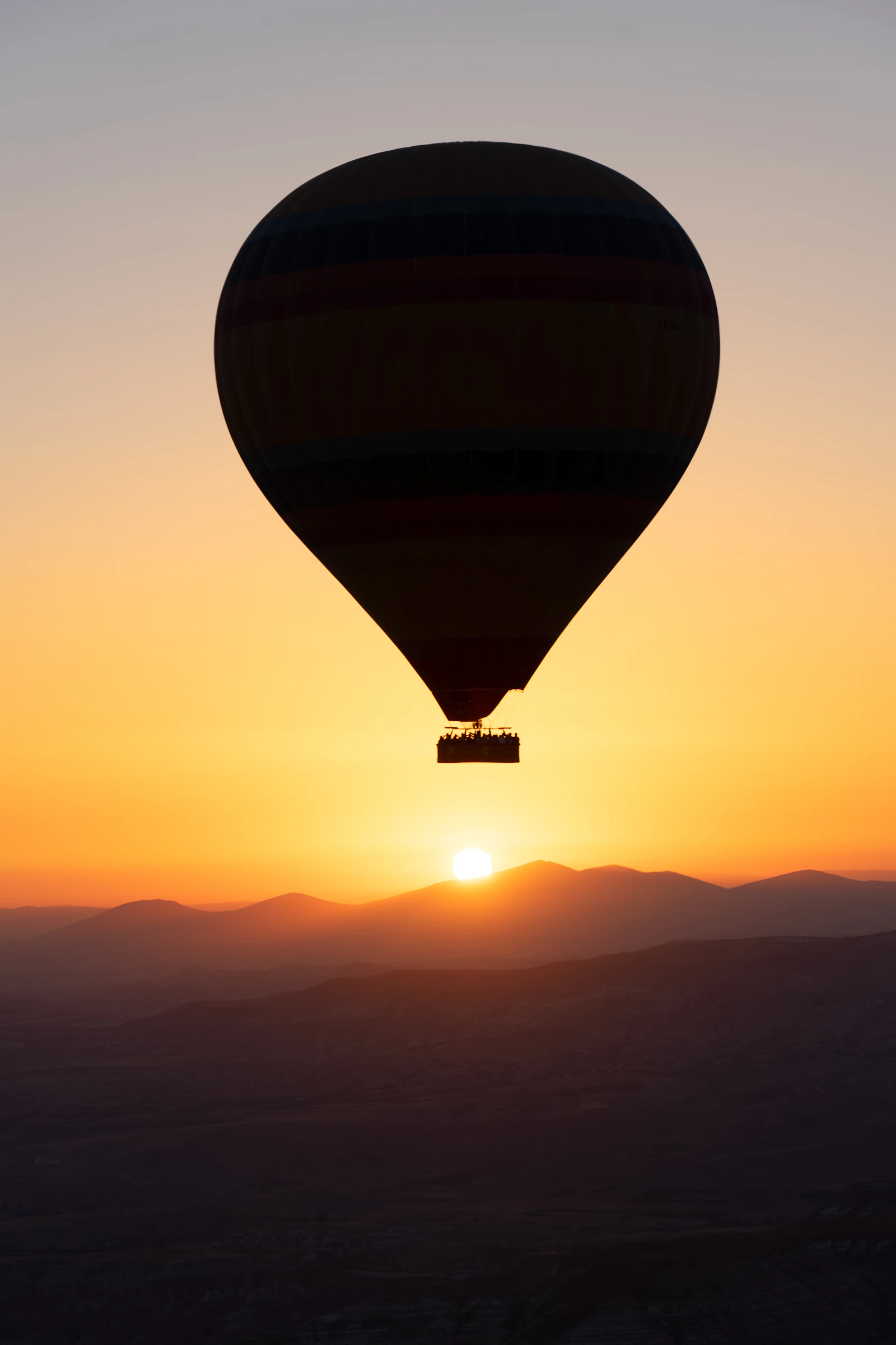 A lone hot air balloon silhouetted above layered hills at sunrise