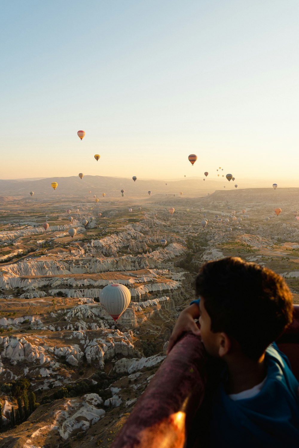 a man looking out over a valley with hot air balloons in the sky