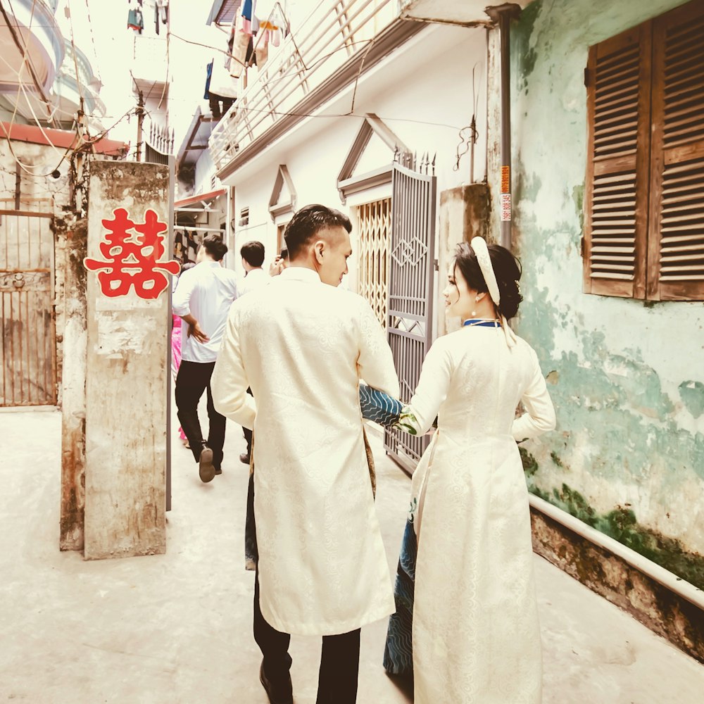 a man and woman dressed in white walking down a street