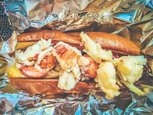 a hot dog with shrimp and potatoes on a piece of tin foil