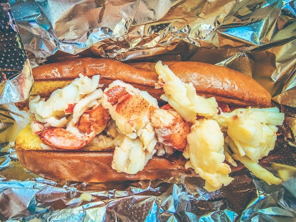 A hot dog with shrimp and potatoes on a piece of tin foil