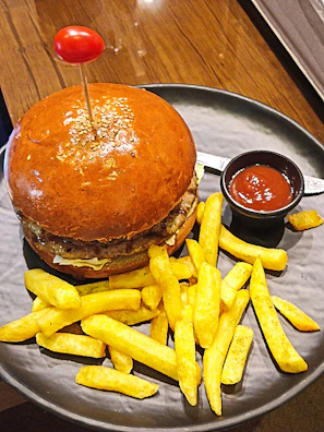 Burger placed on a wooden platter accompanied by fries and a dipping sauce.