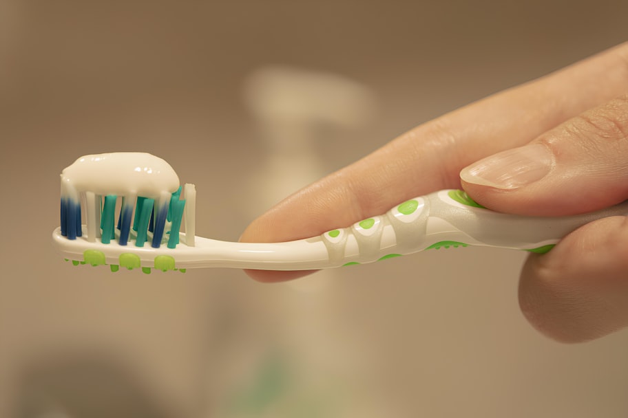 Hand holding a toothbrush with a pea-sized amount of toothpaste applied to soft bristles