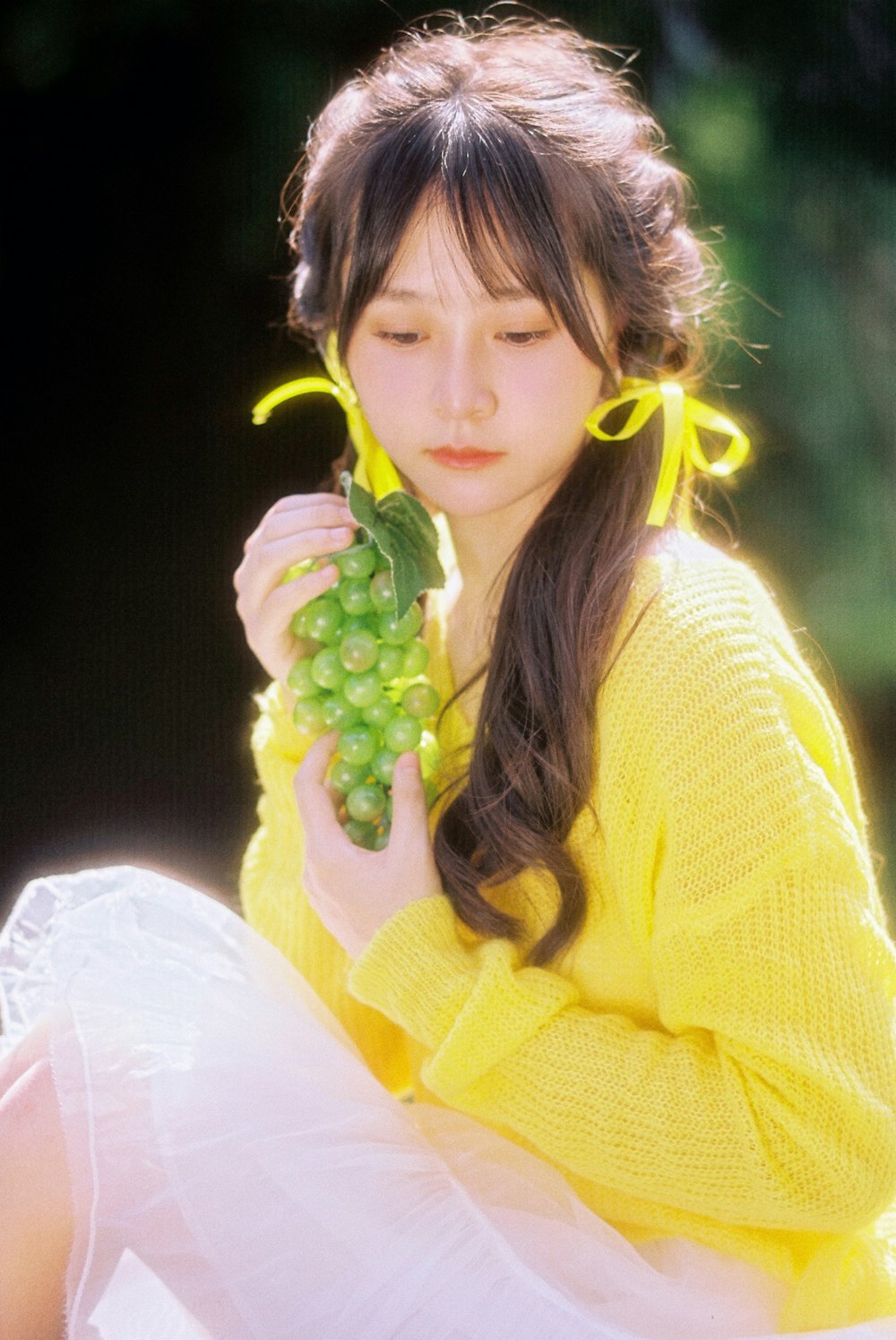 a woman in a yellow sweater holding a bunch of grapes