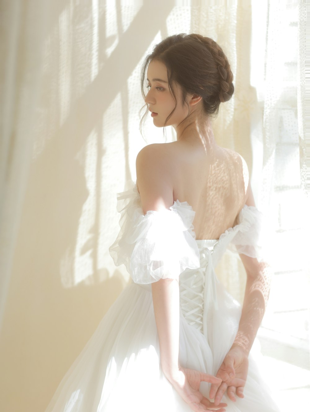 a woman in a white dress standing in front of a window