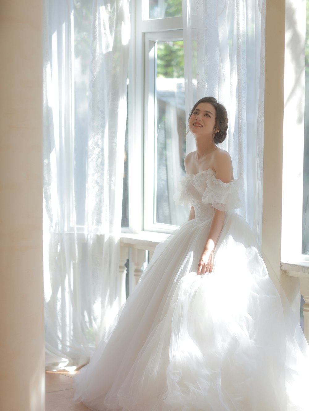 a woman in a wedding dress standing in front of a window