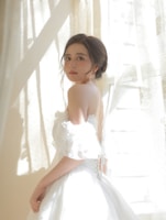 Softly lit photo of a model wearing a flowing neutral-toned dress in a sunlit room.