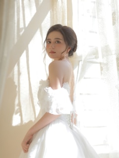 A female model in a blush dress, standing gracefully with soft lighting highlighting her features.