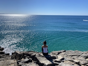 a woman sitting on rocks looking out at the ocean