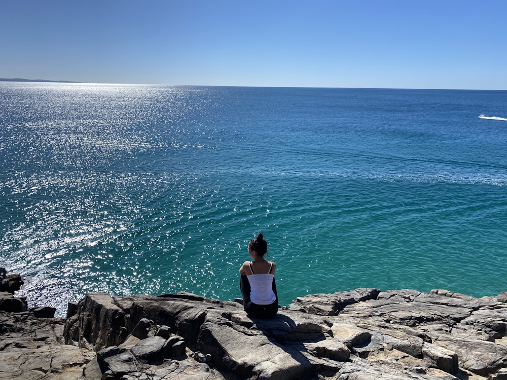 a woman sitting on rocks looking out at the ocean
